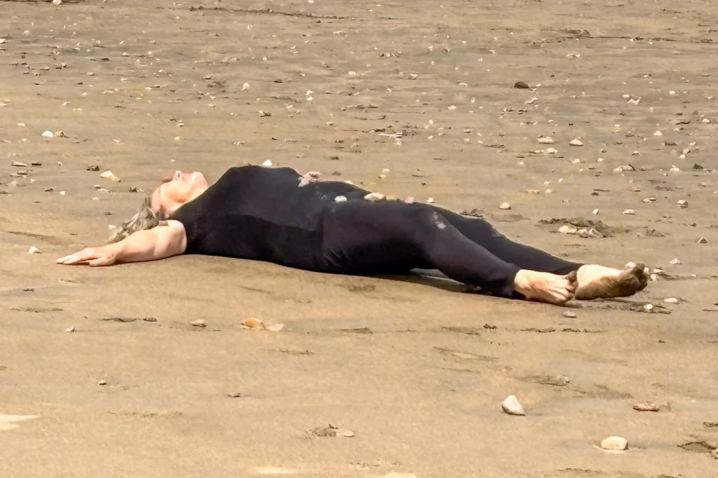 A person in a black outfit lying flat on their back on a sandy beach.