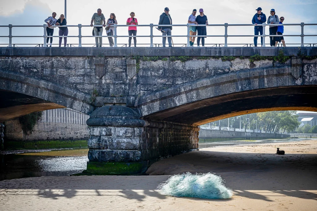 People standing on a stone bridge over a sandy riverbank with a pile of fishing netting in the foreground.